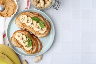 Photo of Tasty sandwiches with peanut butter, banana, chia seeds, nuts and mint on white tiled table, flat lay. Space for text