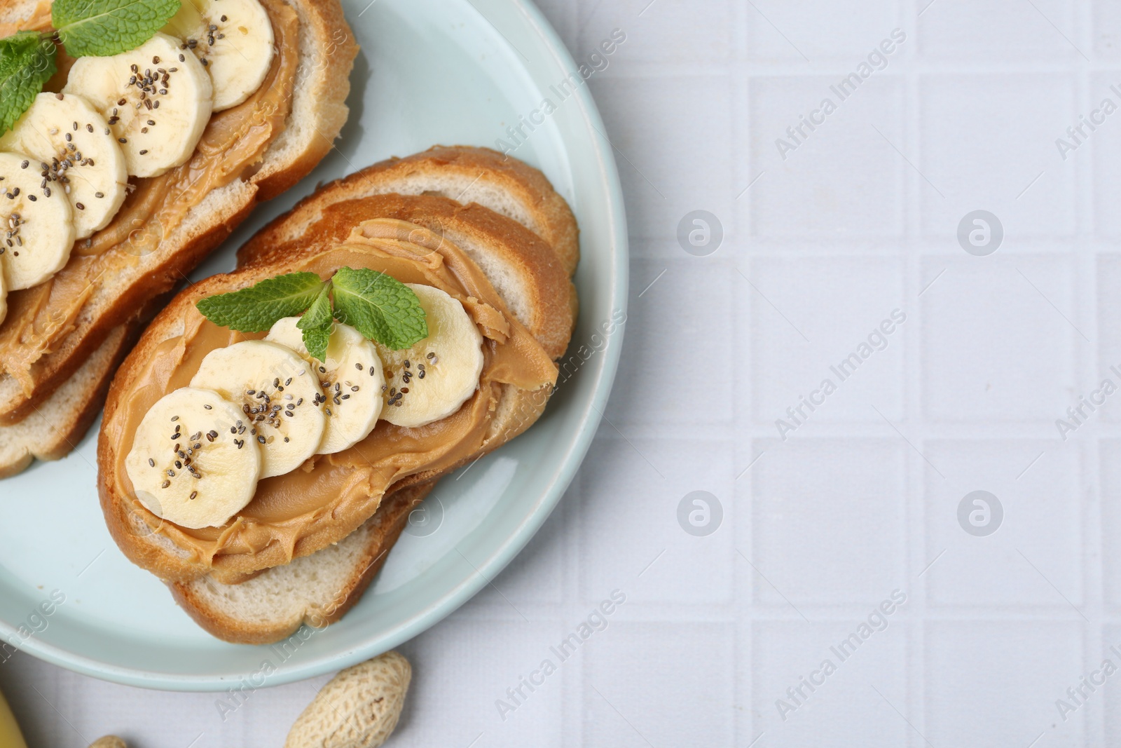 Photo of Tasty sandwiches with peanut butter, banana, chia seeds and mint on white tiled table, top view. Space for text