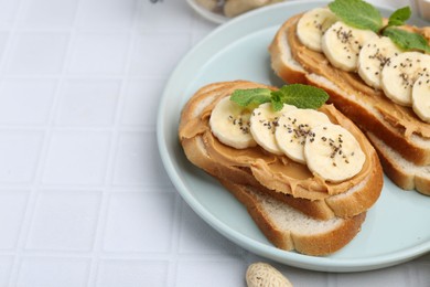 Photo of Tasty sandwiches with peanut butter, banana, chia seeds and mint on white tiled table, closeup. Space for text