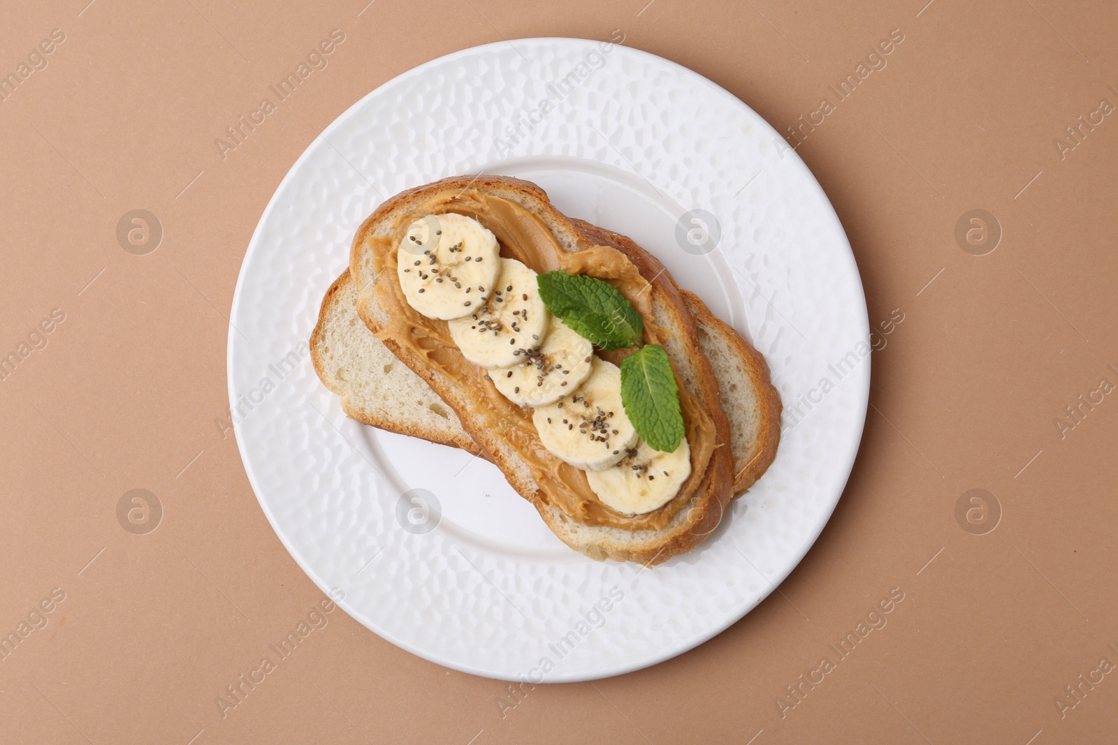 Photo of Tasty sandwich with peanut butter, banana, chia seeds and mint on brown background, top view