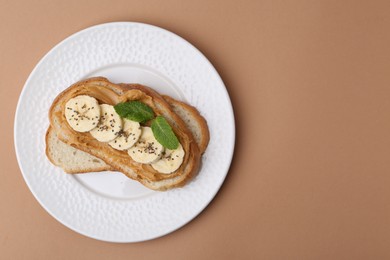 Photo of Tasty sandwich with peanut butter, banana, chia seeds and mint on brown background, top view. Space for text