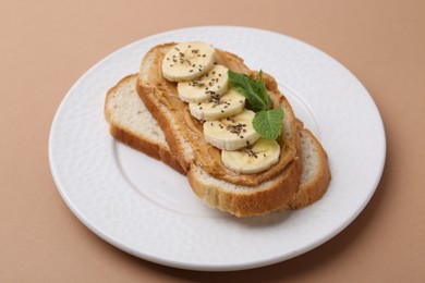 Photo of Tasty sandwich with peanut butter, banana, chia seeds and mint on brown background, closeup