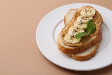 Photo of Tasty sandwich with peanut butter, banana, chia seeds and mint on brown background, closeup. Space for text