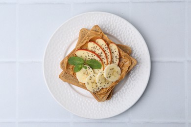 Photo of Tasty sandwich with peanut butter, apples, banana, chia seeds and mint on white tiled table, top view