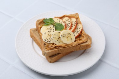 Photo of Tasty sandwich with peanut butter, apple, banana, chia seeds and mint on white table, closeup