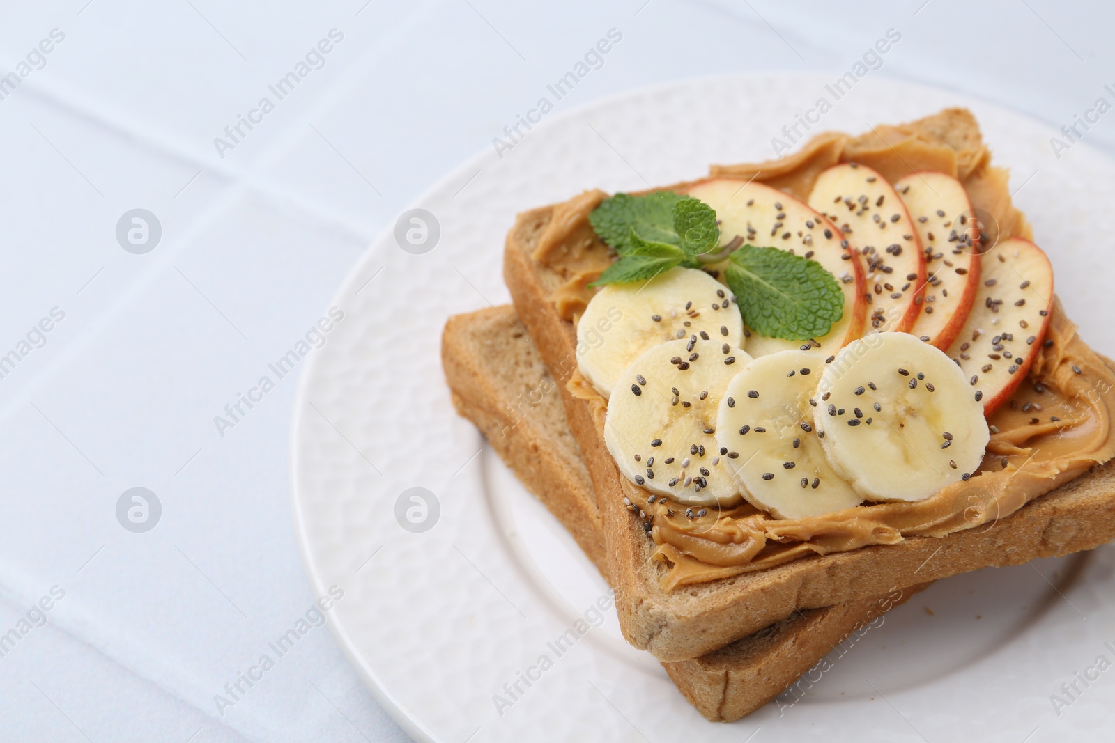 Photo of Tasty sandwich with peanut butter, apple, banana, chia seeds and mint on white table, closeup