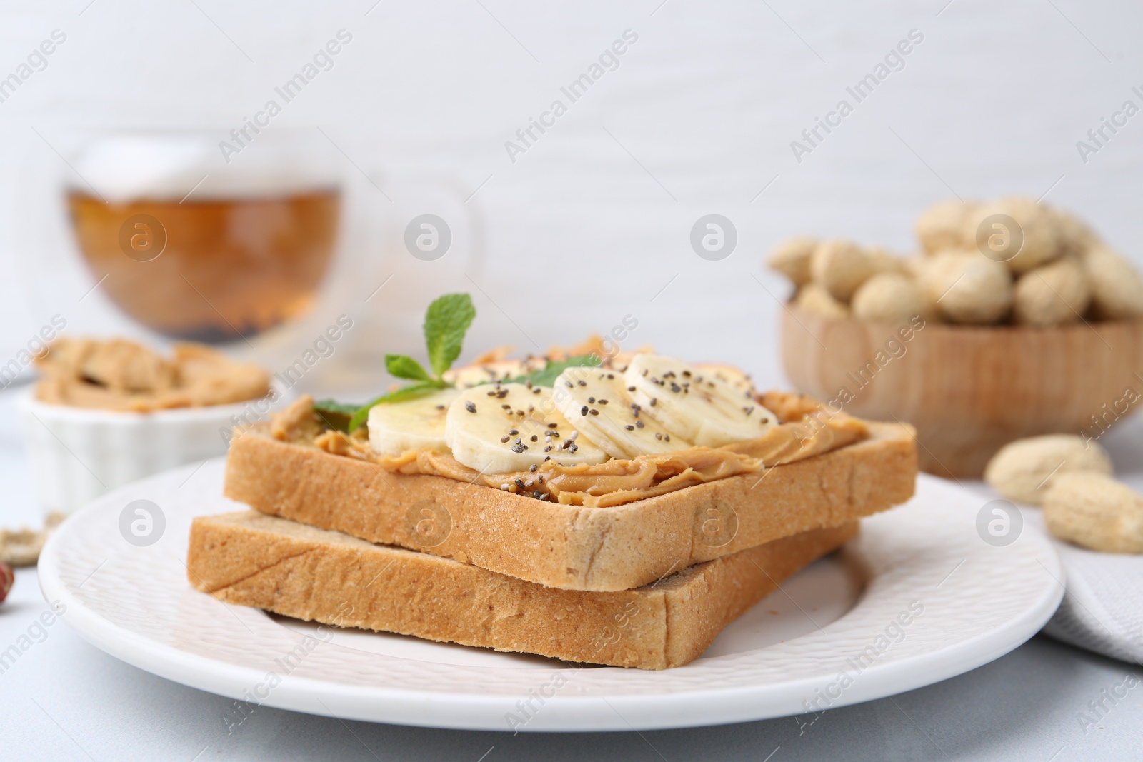 Photo of Tasty sandwich with peanut butter, banana, chia seeds and mint on table, closeup