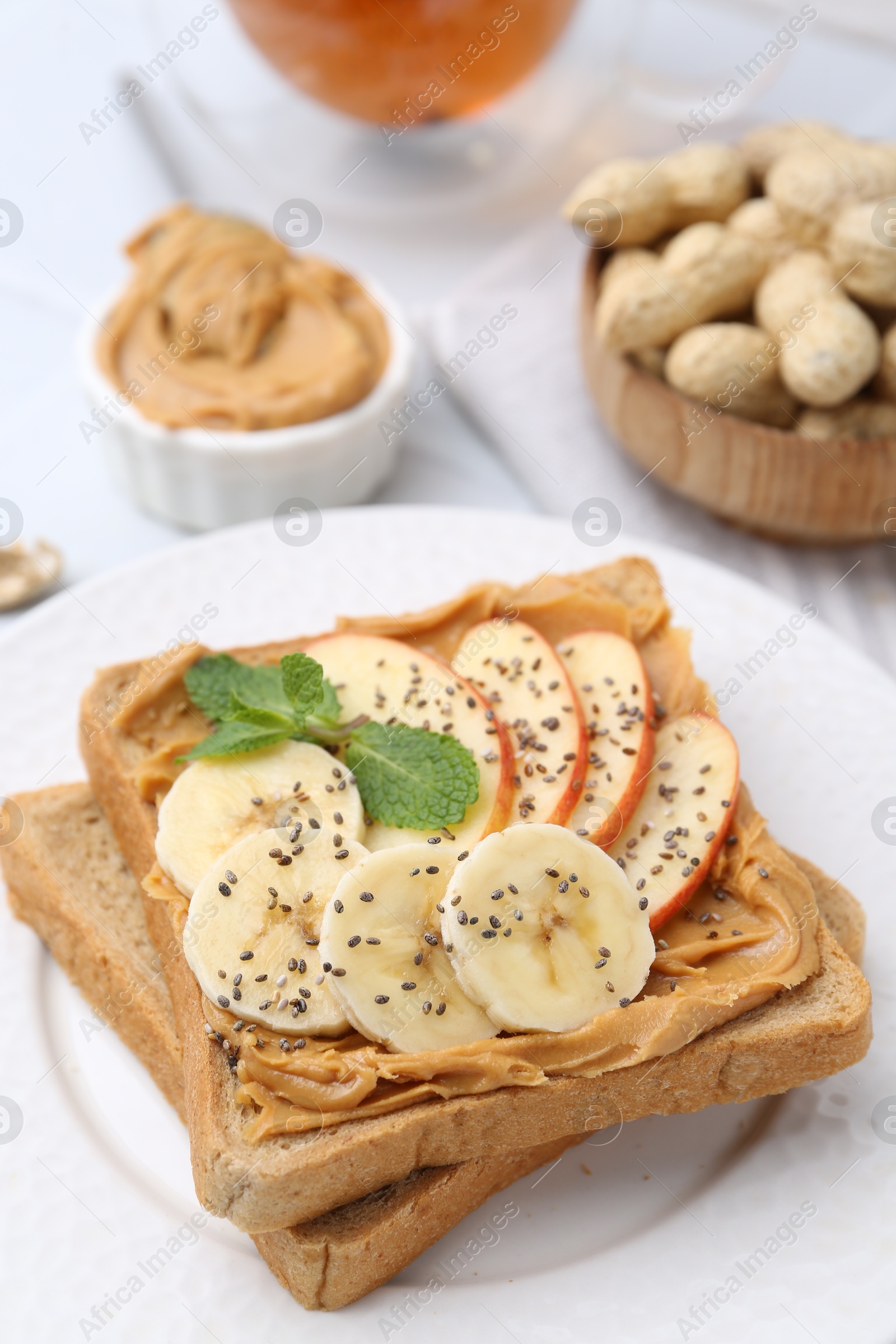 Photo of Tasty sandwich with peanut butter, apple, banana, chia seeds and mint on table, closeup