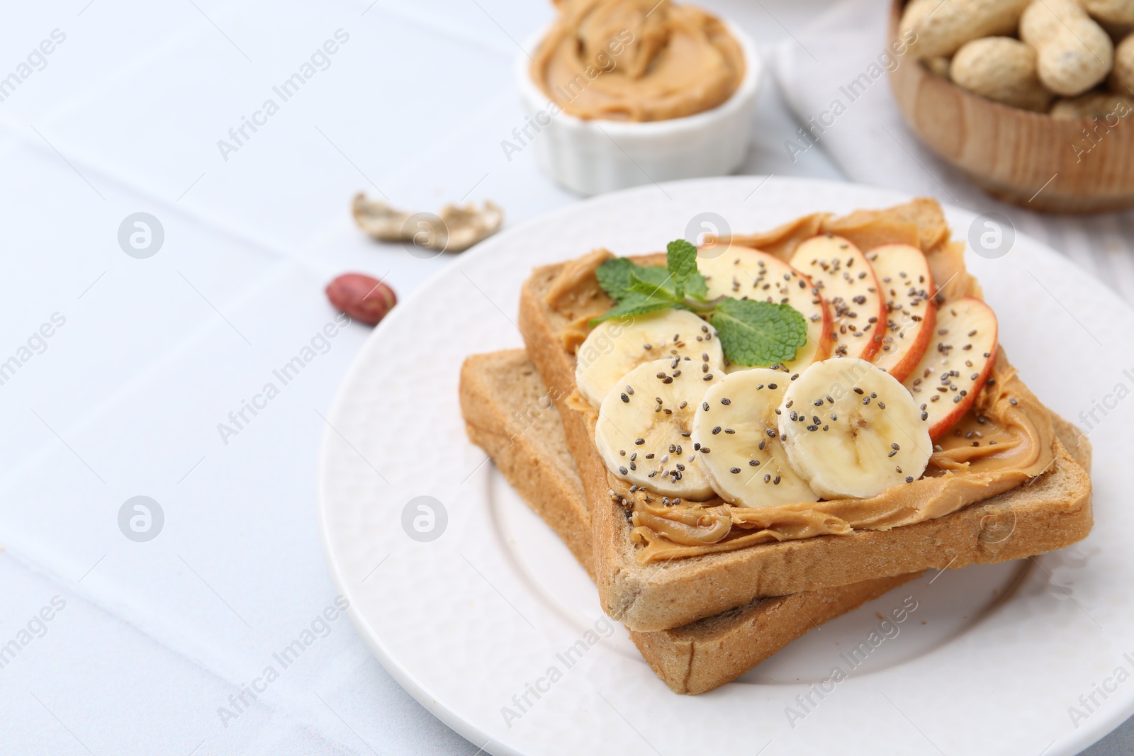 Photo of Tasty sandwich with peanut butter, apple, banana, chia seeds and mint on white table, closeup