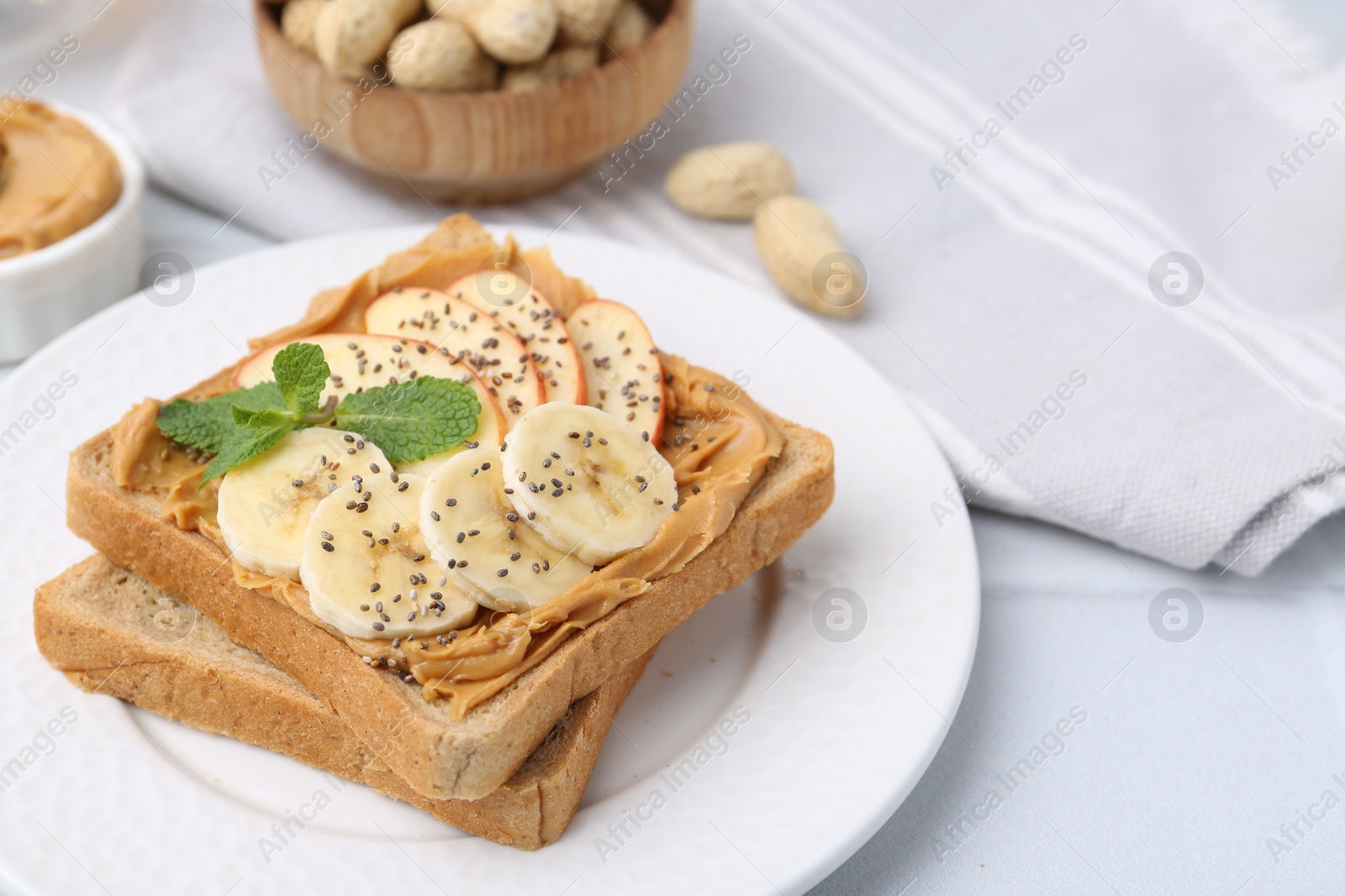 Photo of Tasty sandwich with peanut butter, apple, banana, chia seeds and mint on white table, closeup