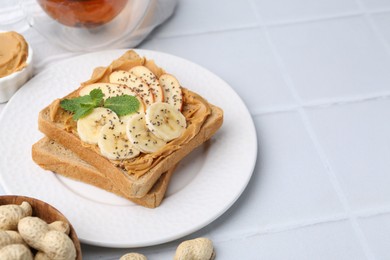 Photo of Tasty sandwich with peanut butter, apple, banana, chia seeds, nuts and mint on white tiled table, closeup. Space for text