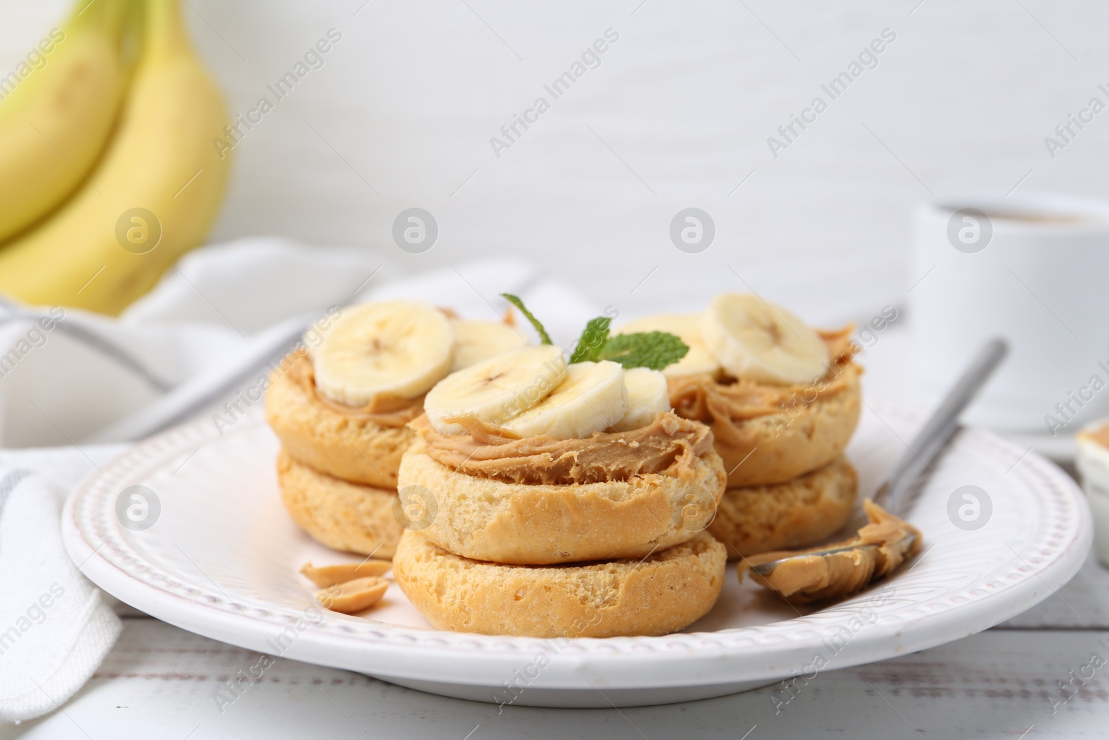 Photo of Tasty sandwiches with peanut butter, banana, mint and spoon on white wooden table, closeup