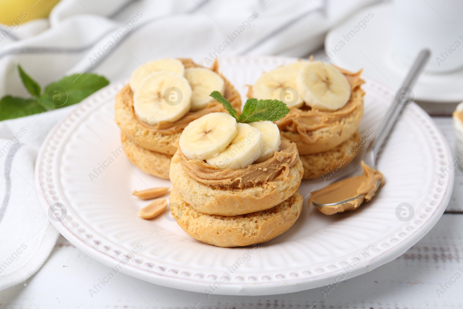 Photo of Tasty sandwiches with peanut butter, banana, mint and spoon on white wooden table, closeup