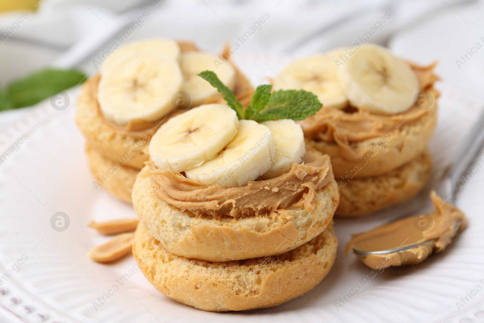 Photo of Tasty sandwiches with peanut butter, banana, mint and spoon on plate, closeup