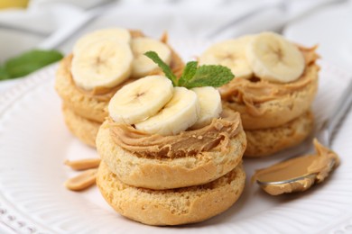 Photo of Tasty sandwiches with peanut butter, banana, mint and spoon on plate, closeup