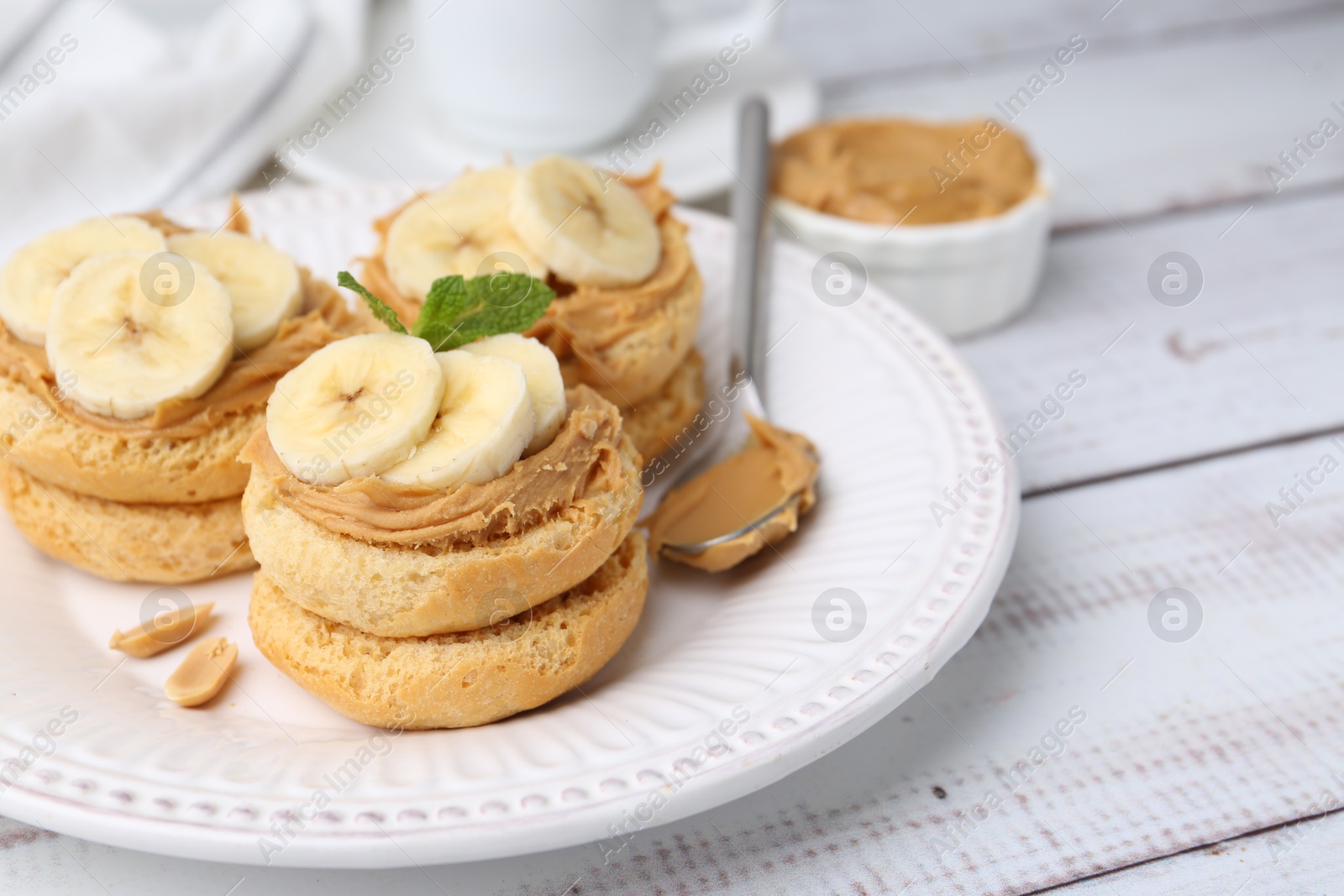 Photo of Tasty sandwiches with peanut butter, banana, mint and spoon on white wooden table, closeup