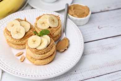 Photo of Tasty sandwiches with peanut butter, banana, mint and spoon on white wooden table, closeup