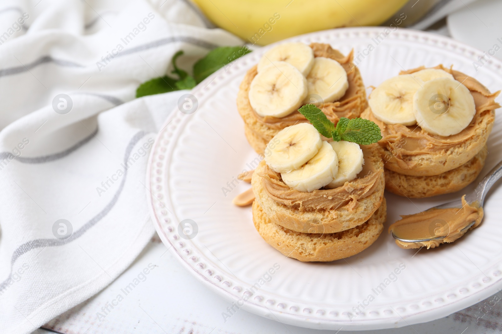 Photo of Tasty sandwiches with peanut butter, banana, mint and spoon on white wooden table, closeup