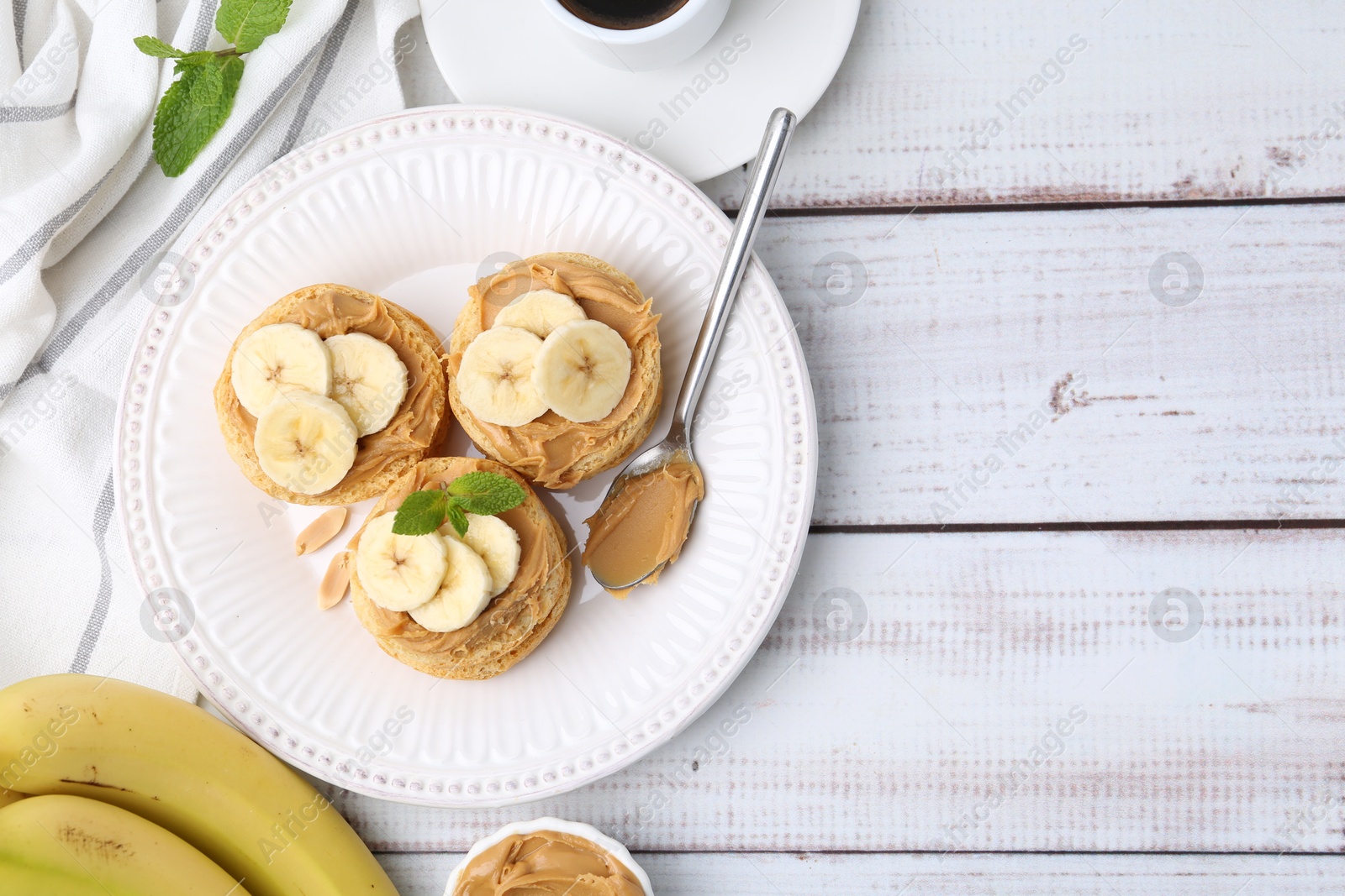 Photo of Tasty sandwiches with peanut butter, banana, mint and spoon on white wooden table, top view. Space for text