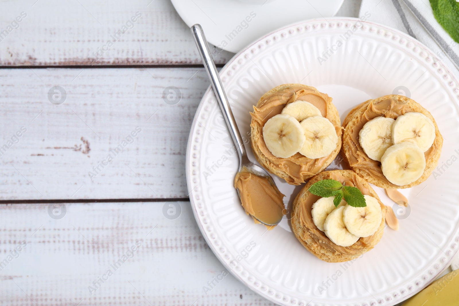 Photo of Tasty sandwiches with peanut butter, banana, mint and spoon on white wooden table, top view. Space for text