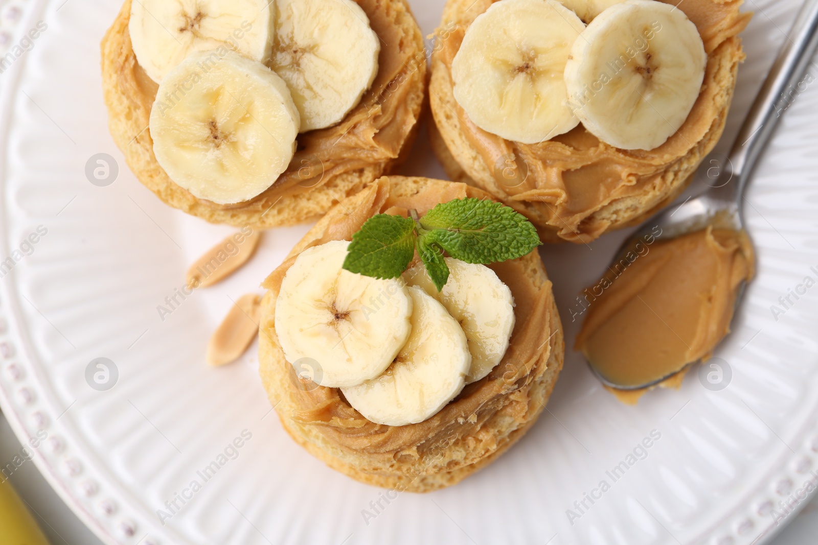 Photo of Tasty sandwiches with peanut butter, banana, mint and spoon on table, top view