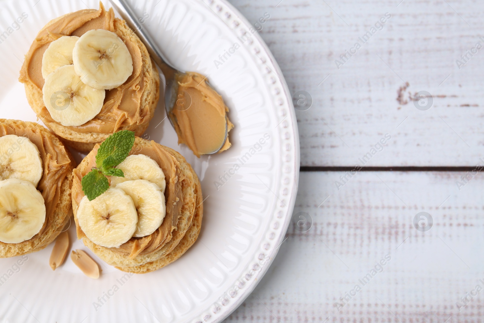 Photo of Tasty sandwiches with peanut butter, banana, mint and spoon on white wooden table, top view. Space for text