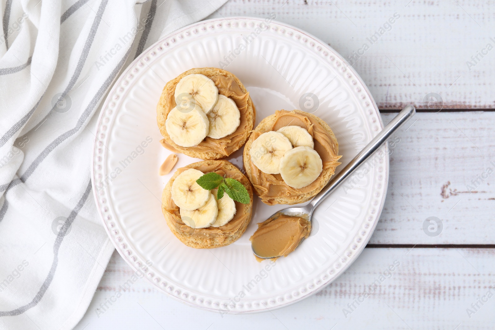 Photo of Tasty sandwiches with peanut butter, banana, mint and spoon on white wooden table, top view