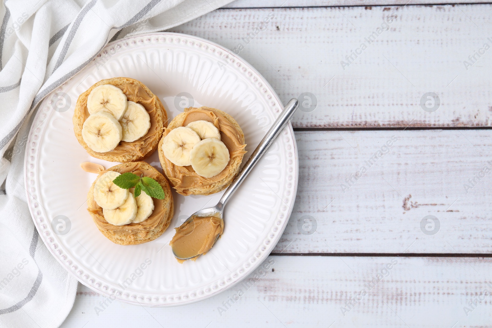 Photo of Tasty sandwiches with peanut butter, banana, mint and spoon on white wooden table, top view. Space for text