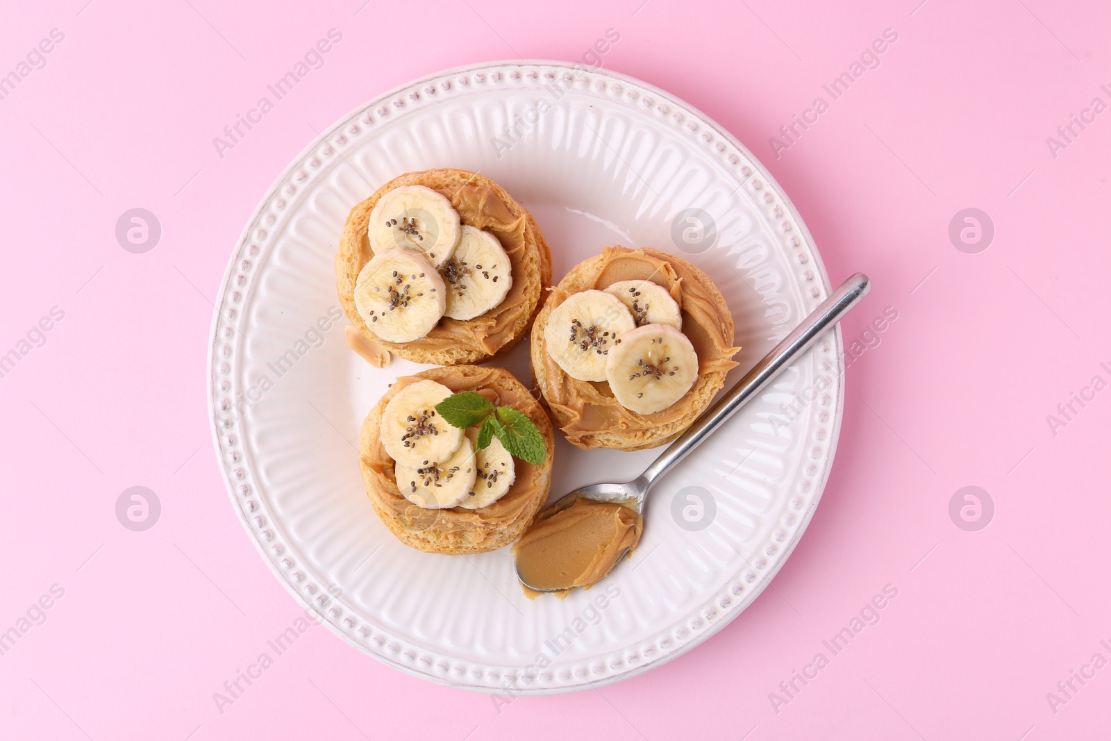 Photo of Tasty sandwiches with peanut butter, banana, chia seeds, mint and spoon on pink background, top view