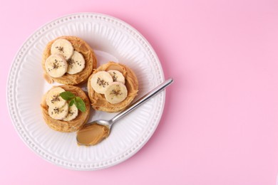 Photo of Tasty sandwiches with peanut butter, banana, chia seeds, mint and spoon on pink background, top view. Space for text