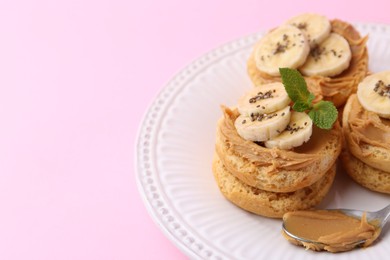 Photo of Tasty sandwiches with peanut butter, banana, chia seeds, mint and spoon on pink background, closeup. Space for text