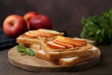 Photo of Tasty sandwiches with peanut butter, apples and mint on wooden table, closeup