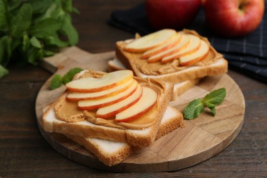 Photo of Tasty sandwiches with peanut butter, apples and mint on wooden table, closeup