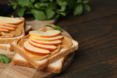 Photo of Tasty sandwiches with peanut butter, apple and mint on wooden table, closeup. Space for text