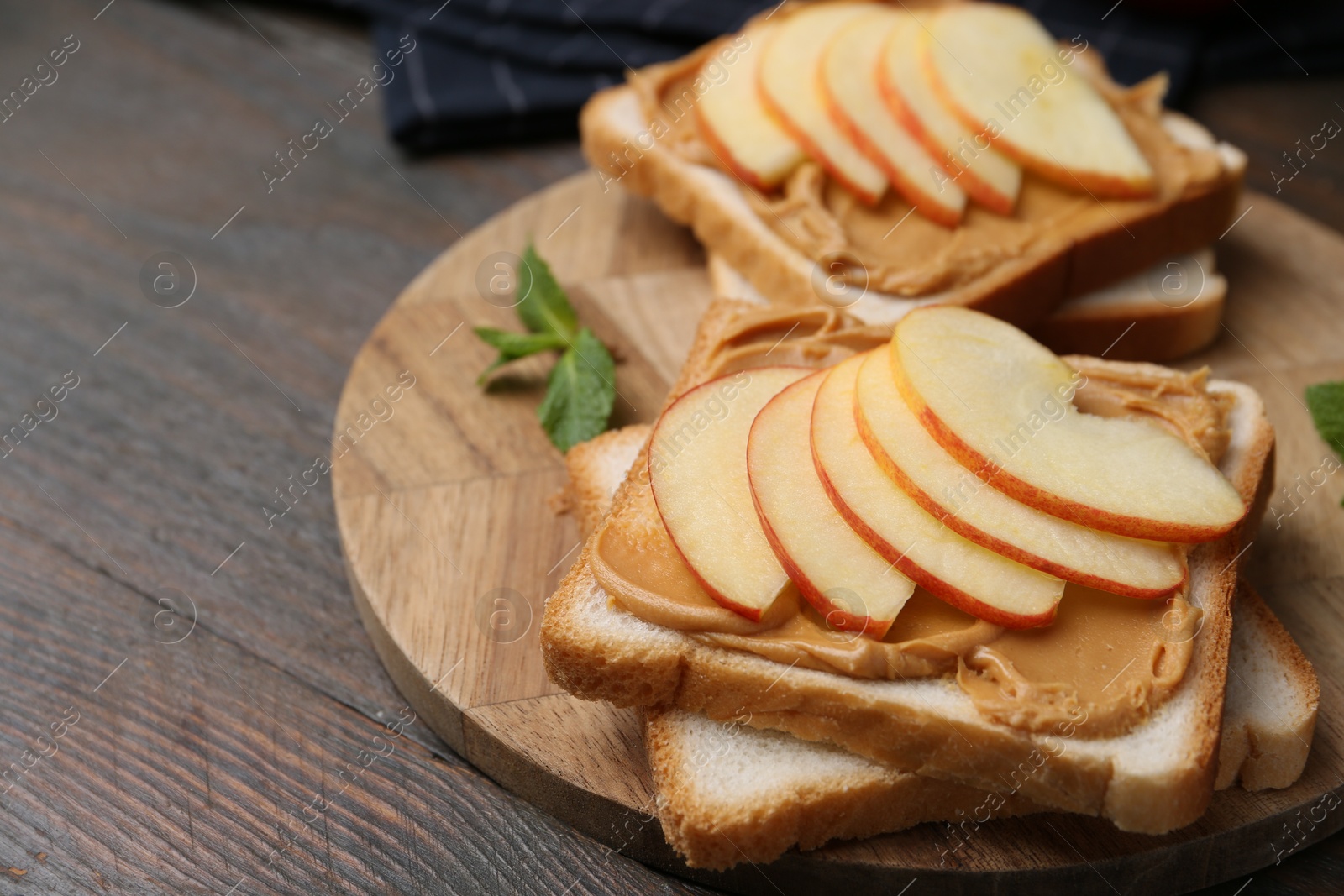 Photo of Tasty sandwiches with peanut butter, apple and mint on wooden table, closeup