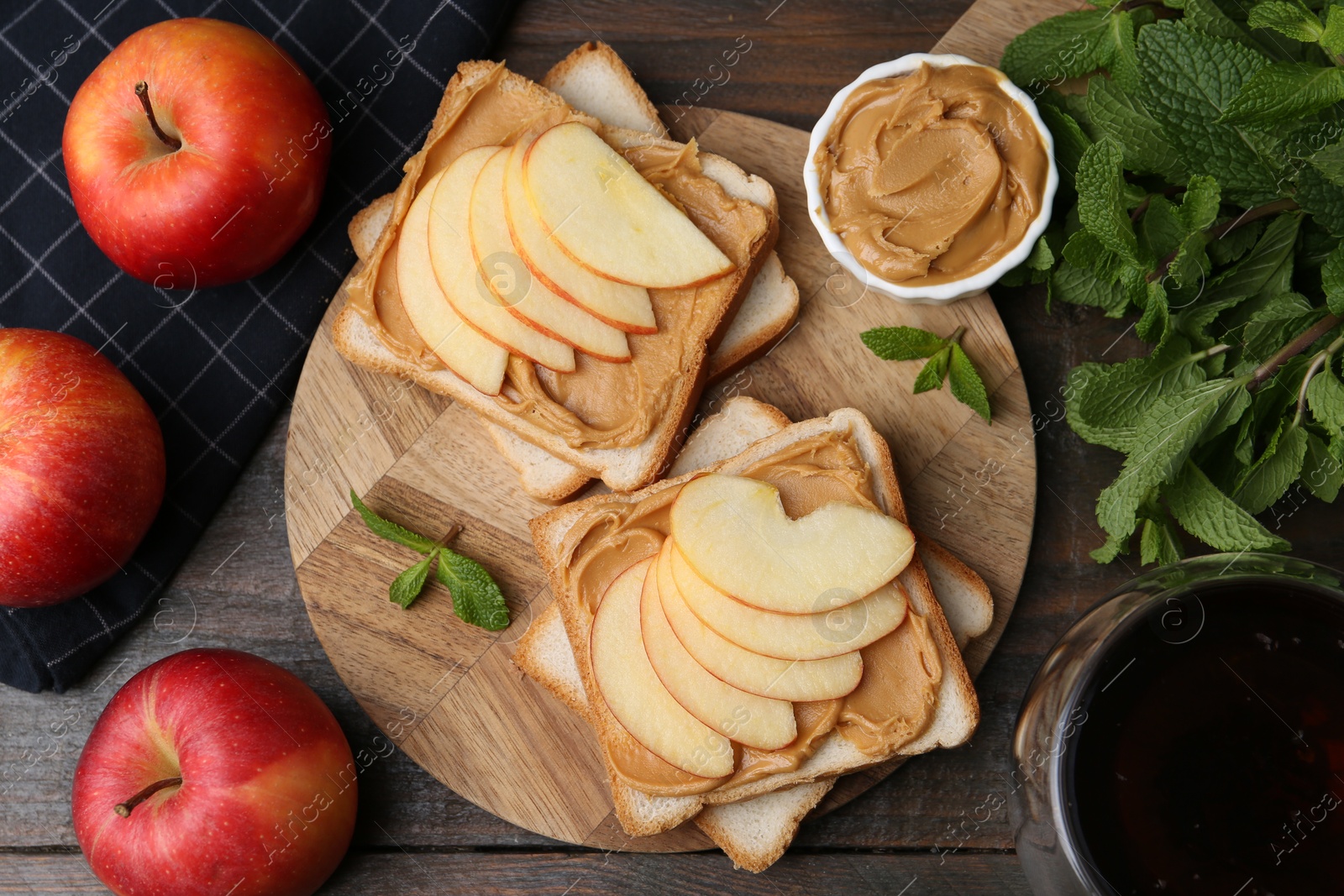 Photo of Tasty sandwiches with peanut butter, apples, mint and tea on wooden table, flat lay