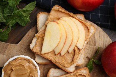 Photo of Tasty sandwiches with peanut butter, apples and mint on wooden table, flat lay