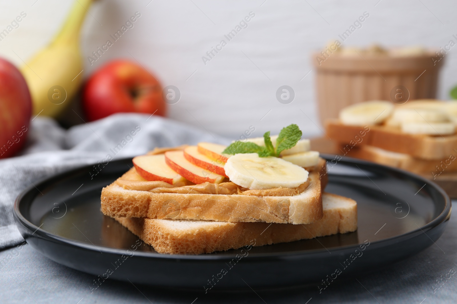 Photo of Tasty sandwich with peanut butter, apple, banana and mint on grey table, closeup