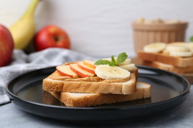 Photo of Tasty sandwich with peanut butter, apple, banana and mint on grey table, closeup