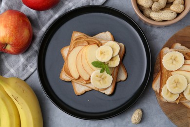 Photo of Tasty sandwiches with peanut butter, apples, bananas, nuts and mint on grey table, flat lay