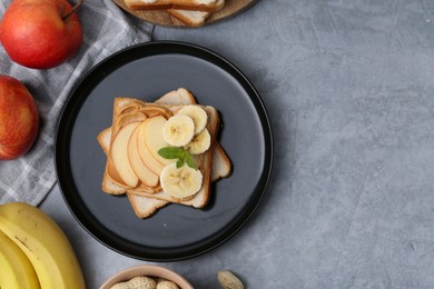 Photo of Tasty sandwich with peanut butter, apples, bananas and mint on grey table, flat lay. Space for text