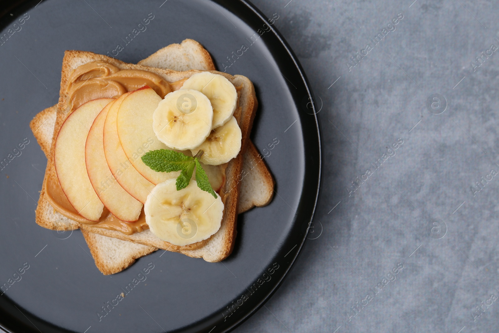 Photo of Tasty sandwich with peanut butter, apple, banana and mint on grey table, top view. Space for text