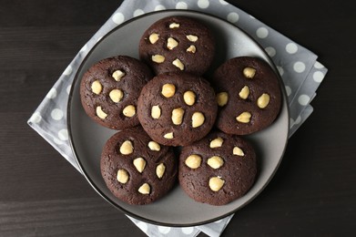 Photo of Delicious chocolate cookies with hazelnuts on black wooden table, top view