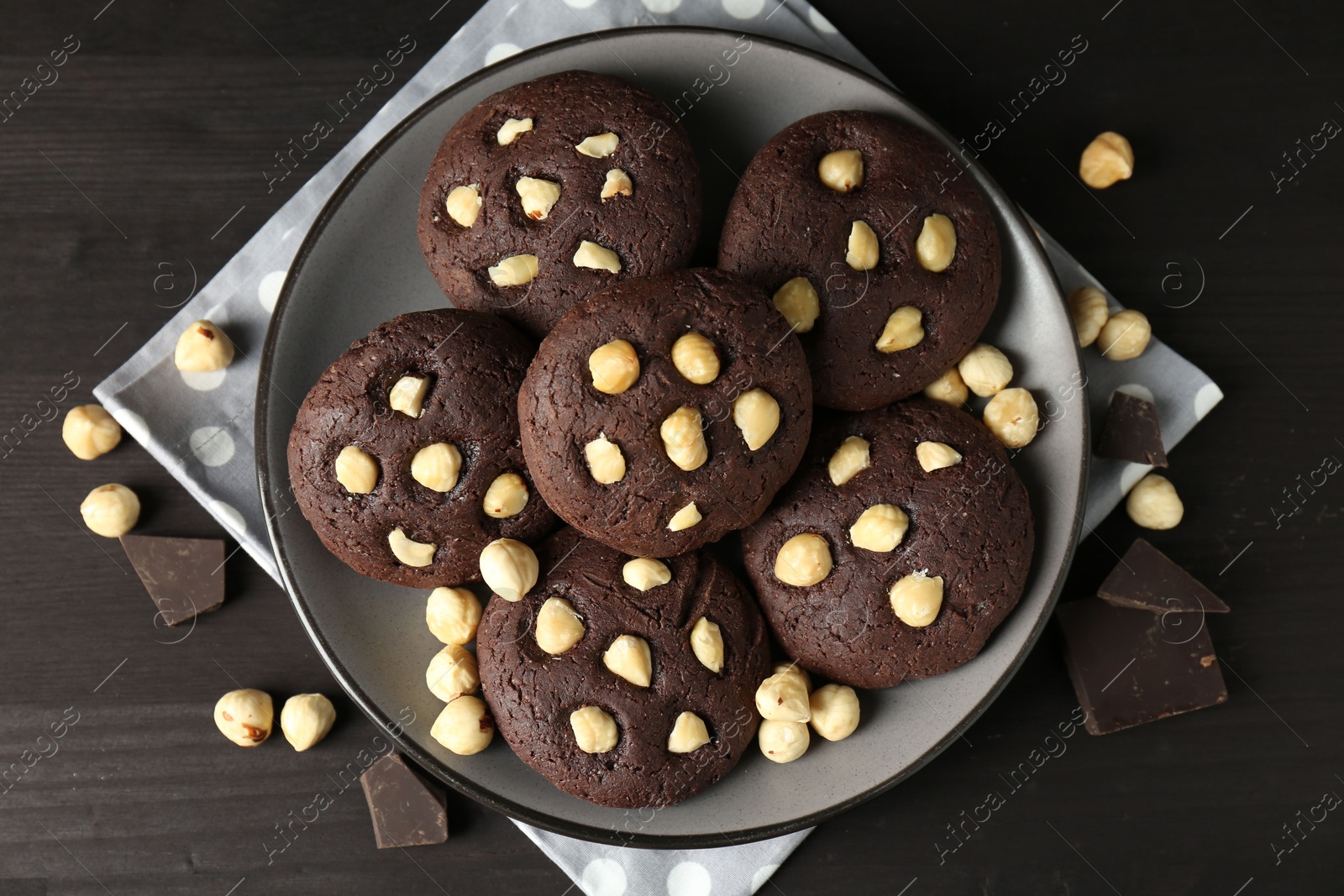 Photo of Delicious chocolate cookies with hazelnuts on black wooden table, flat lay