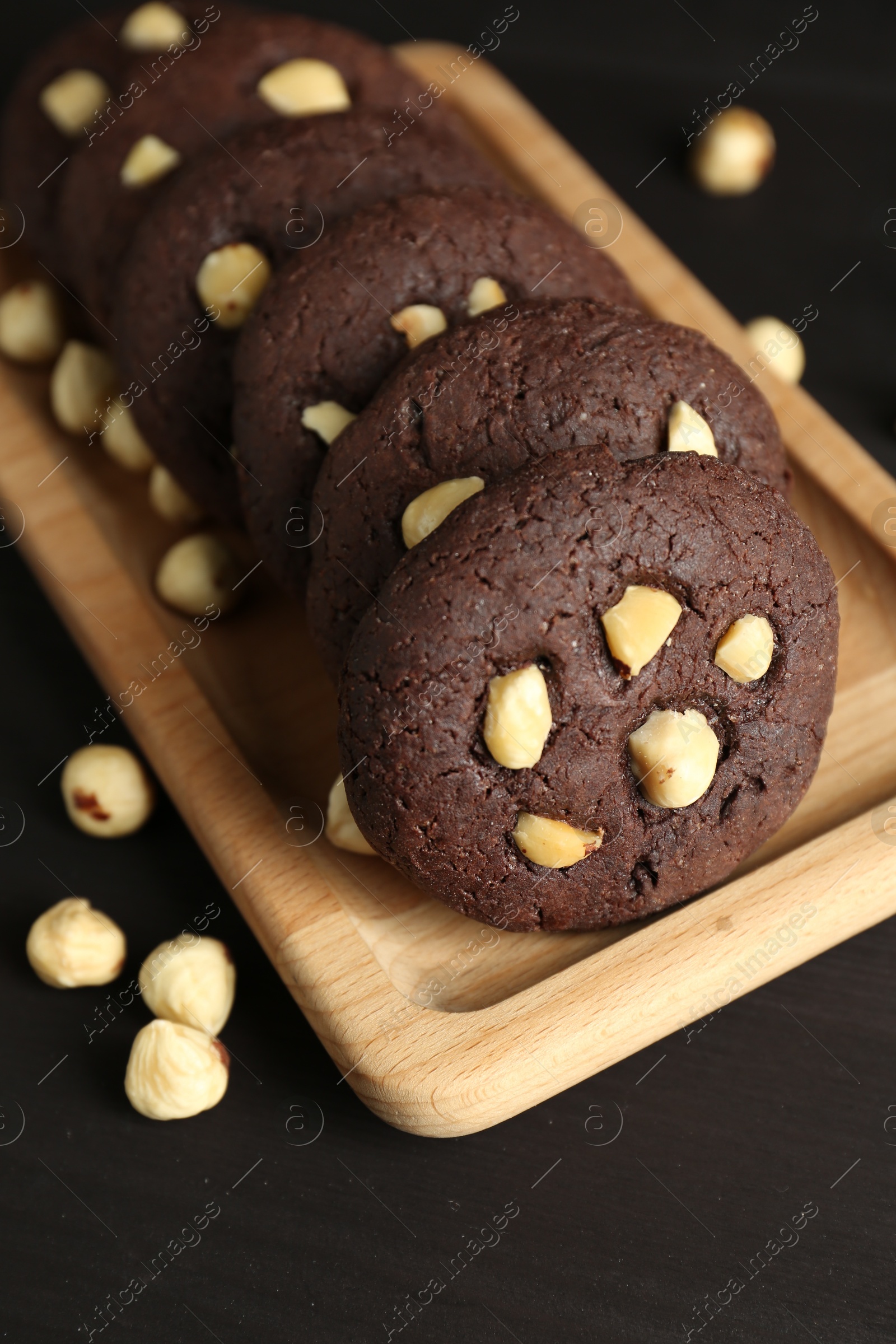 Photo of Delicious chocolate cookies with hazelnuts on black wooden table, closeup