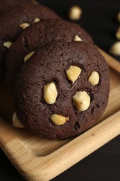 Photo of Delicious chocolate cookies with hazelnuts on black table, closeup