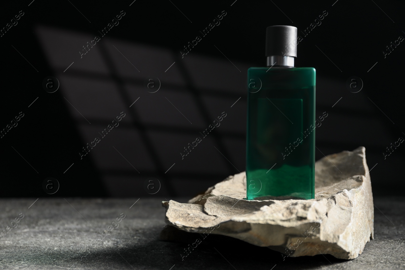 Photo of Bottle of fragrant perfume and rock on grey table, space for text