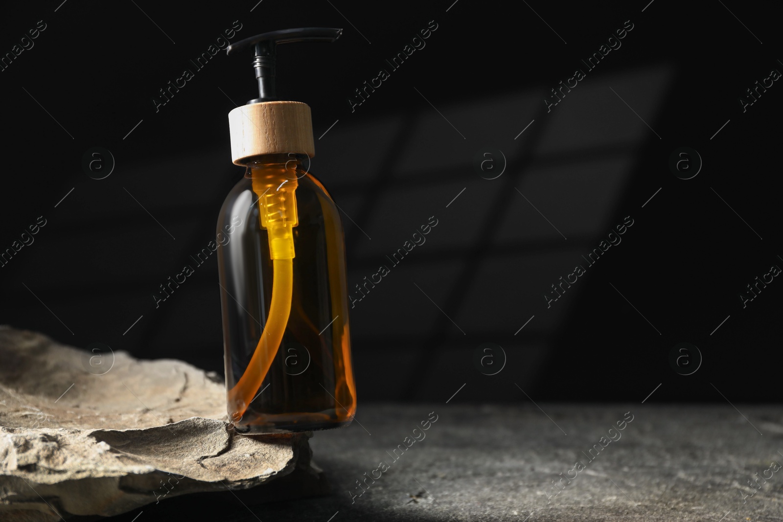 Photo of Bottle of cosmetic product and rock on grey table, space for text