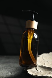 Photo of Bottle of cosmetic product and rock on grey table, closeup