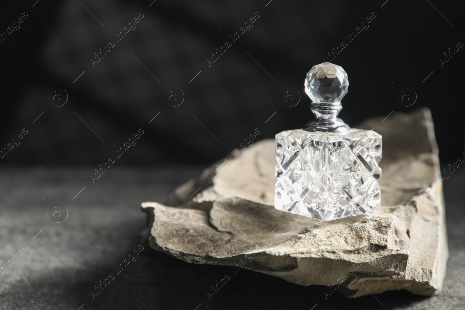 Photo of Bottle of fragrant perfume and rock on grey table, space for text